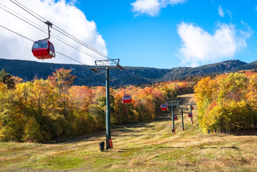 Overhead cable car over a forested slope to a mountain peak on a sunny day. Stowe, VT, USA.