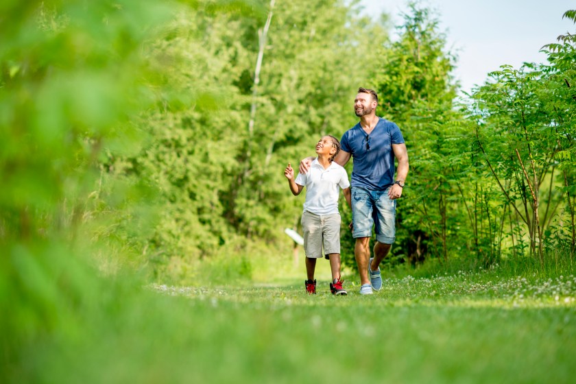 A multi-ethnic family, father and son, going for a walk through nature in a park.