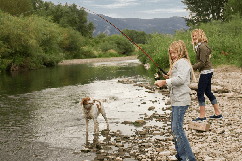 Sisters fishing by river with family dog