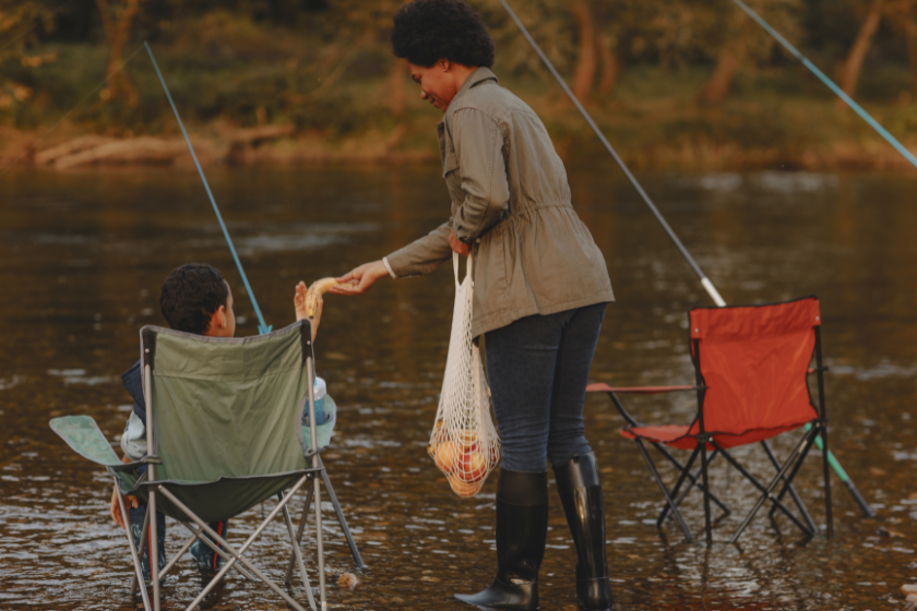 Happy little family enjoying snack while fishing. Sitting in the river on fishing chairs with fishing rods in water