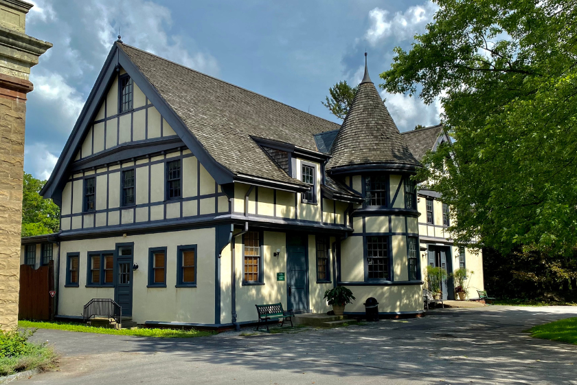 house with prominent tent-roofed turret, half-timbered stucco façade, and the prominent bargeboards on the gables, the Carriage House at Sonnenberg Gardens State Historic Park.