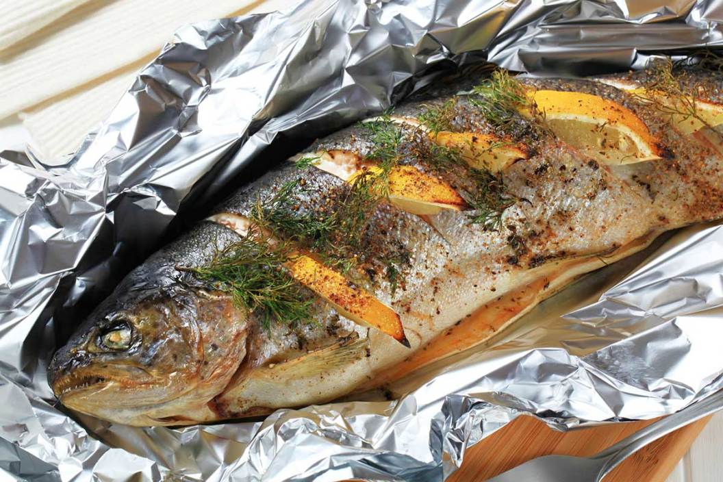 A stuffed trout with dill and lemons sitting in aluminum foil