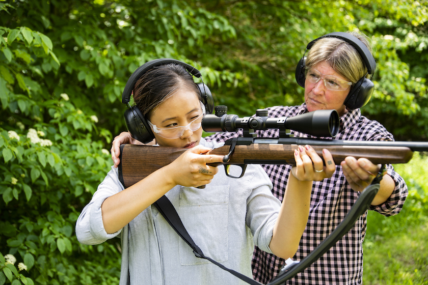 A young woman being taught by a female instructor on how to shoot a rifle.