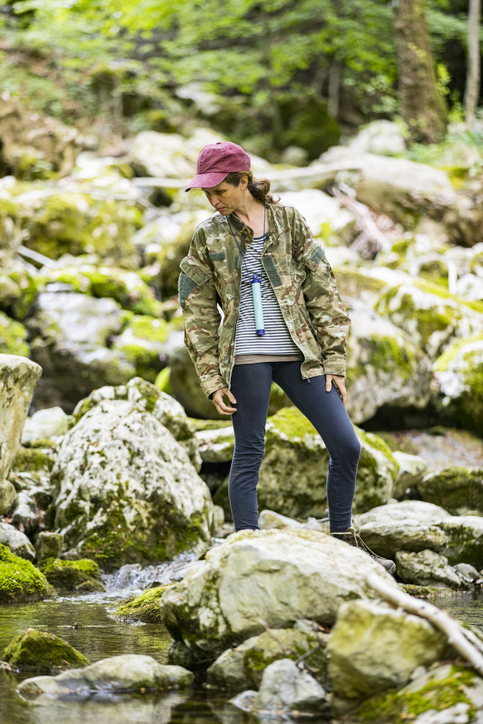 Mid Adult Woman Exploring Streams in Forest Having Water Filtration Straw With Her.