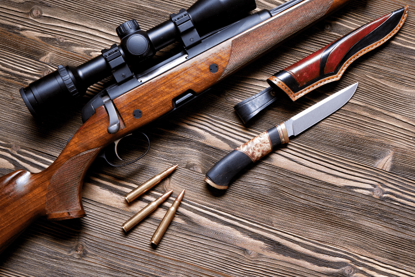 A gun with an optical sight, a hunting knife on a wooden background.Top view.