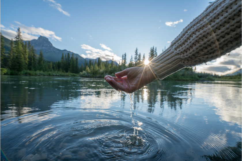 Human hand cupped to catch the fresh water from the river, reflection on water surface