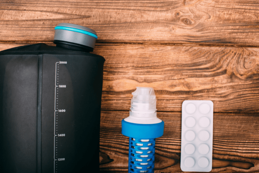 kit for water purification during the hiking. Items include filter for water purification, tablets and a bottle for water on wooden background top view