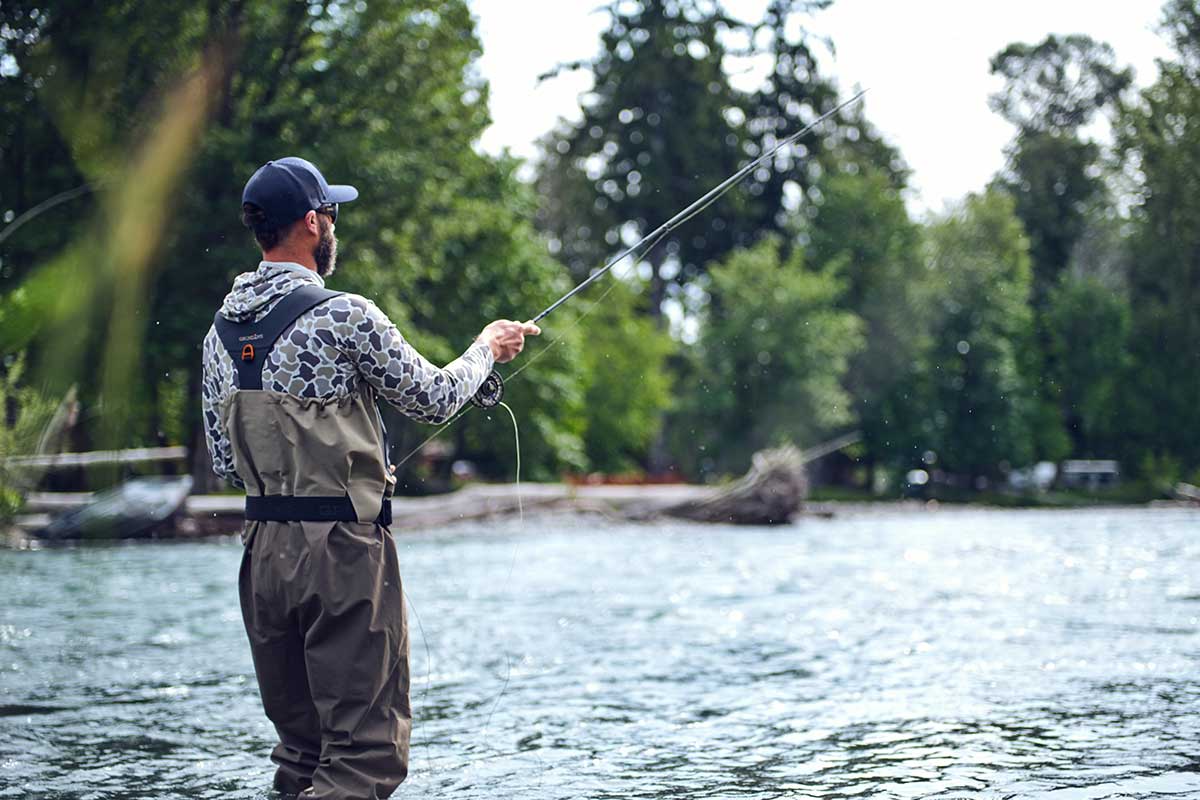 Man standing in a river fishing while wearing Grundéns waders.