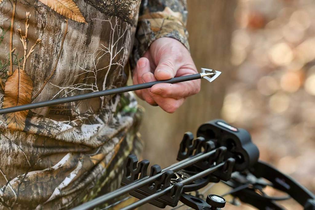 Archery hunter holds an arrow in his hands.