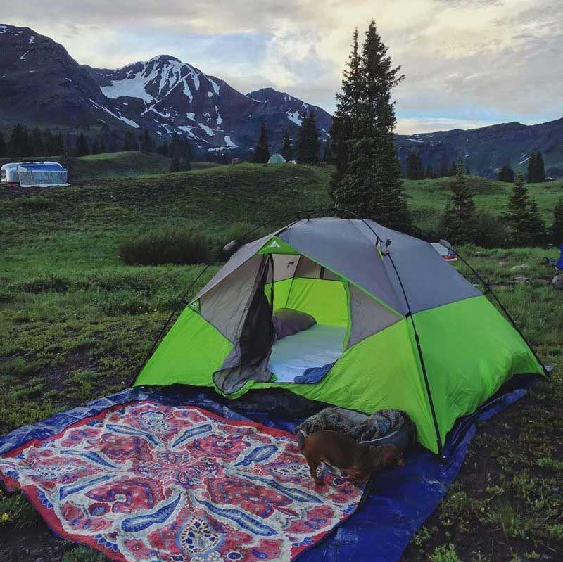 Tarpestry, and outdoor blanket, laying outside a tent in a campground with a mountain in the background