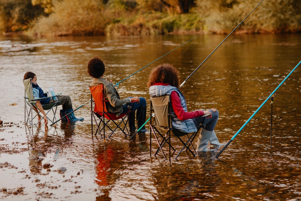 Family sitting in camping chairs, relaxing by the river and fishing