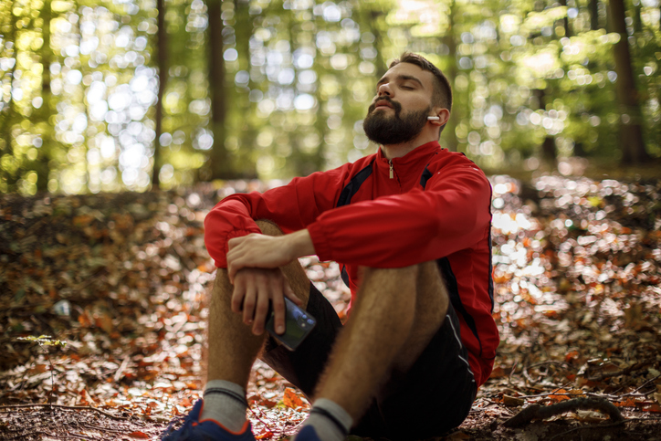 Portrait of relaxed young man with bluetooth headphones in forest