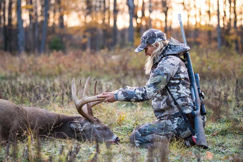 A woman kneels near a deer that she just harvested.