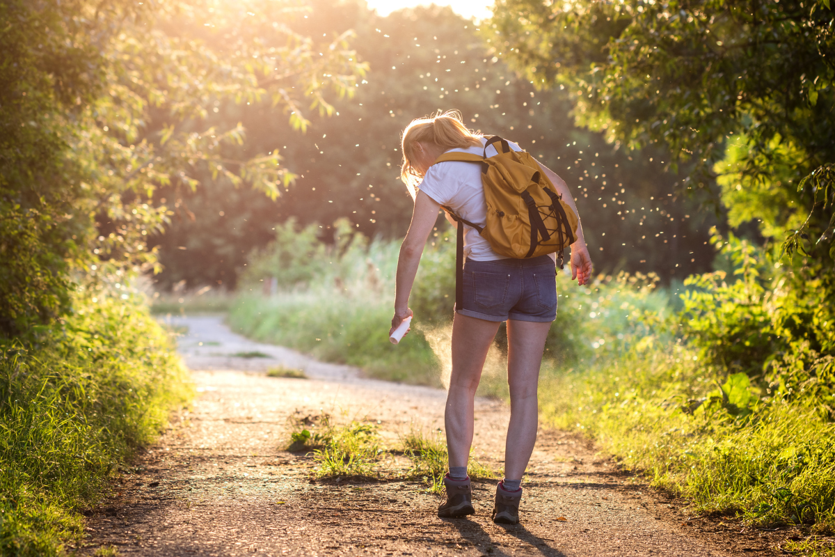 Woman applying insect repellent against mosquito and tick on her leg during hike in nature. Skin protection against insect bite