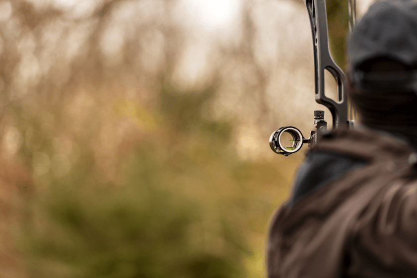 Close-up of an archer, back view, while aiming with a hunting compound bow, with blurred vegetation in the background