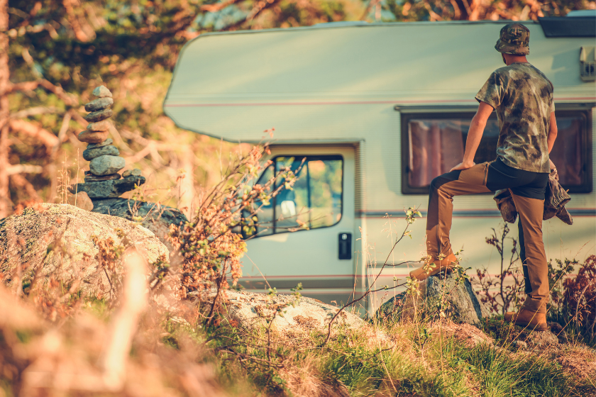 Caucasian Tourist Wearing Camouflage T-Shirt and Hat in Front of His Camper Van RV Motorhome. Road Trip.