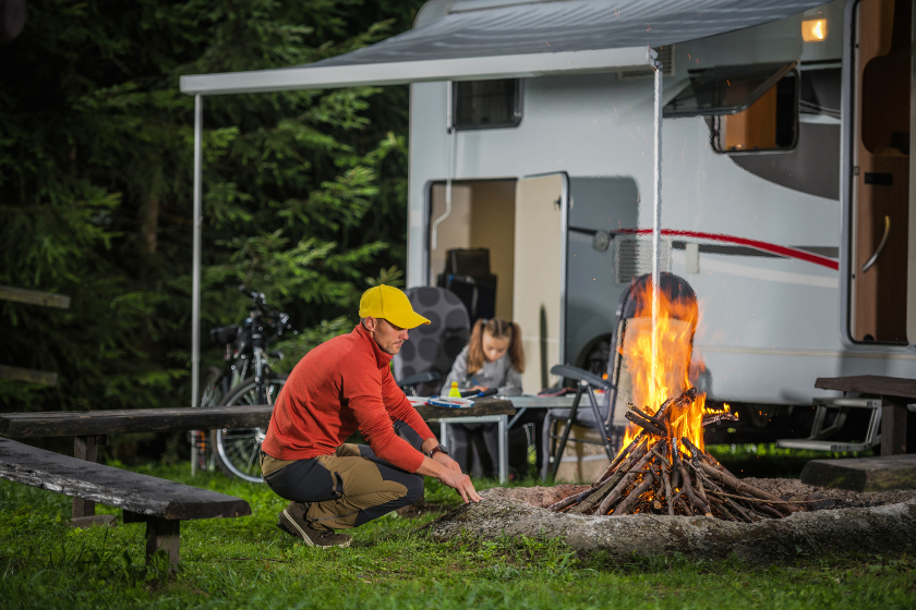 Caucasian Family on the Summer Camping. Father Spending Time Near Campfire. His Daughter Writing Vacation Destination Letter Next to RV Camper Van.