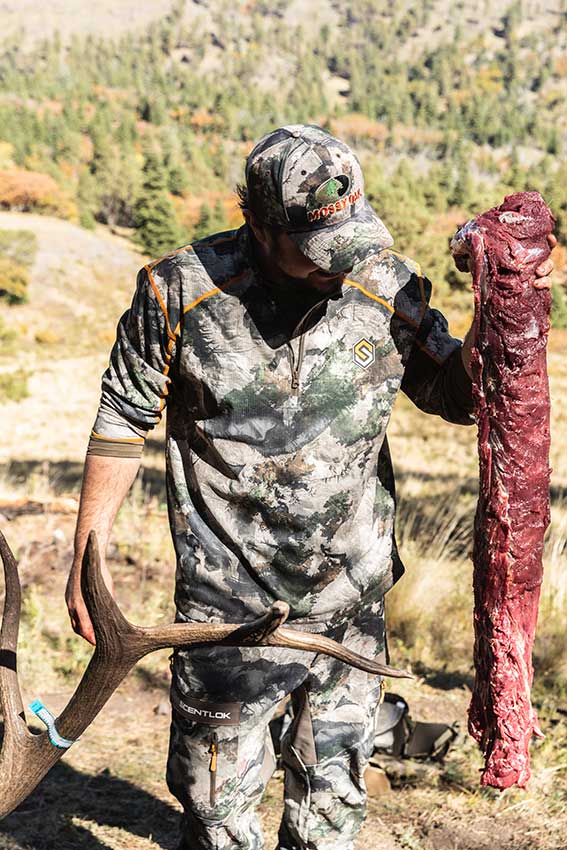 Hunter holding an elk backstrap, or tenderloin, while field dressing the animal.