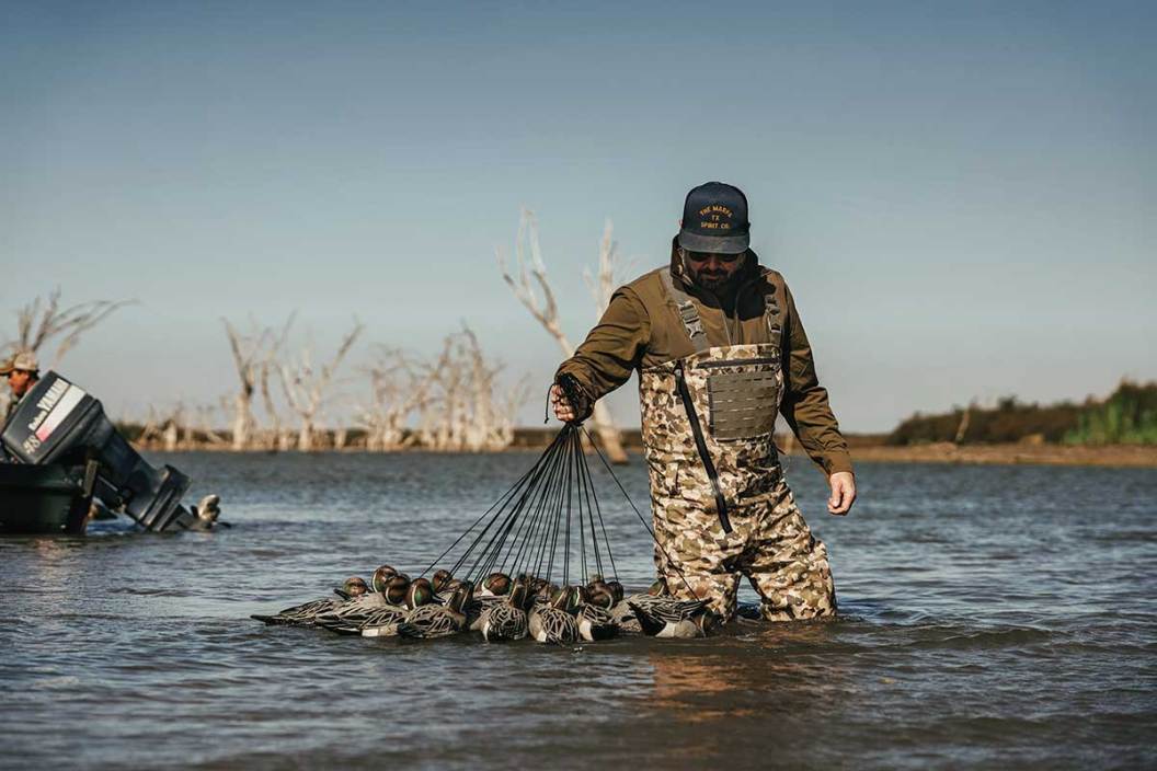 The new Duck Camp Zip Waders worn by a hunter holding duck decoys.