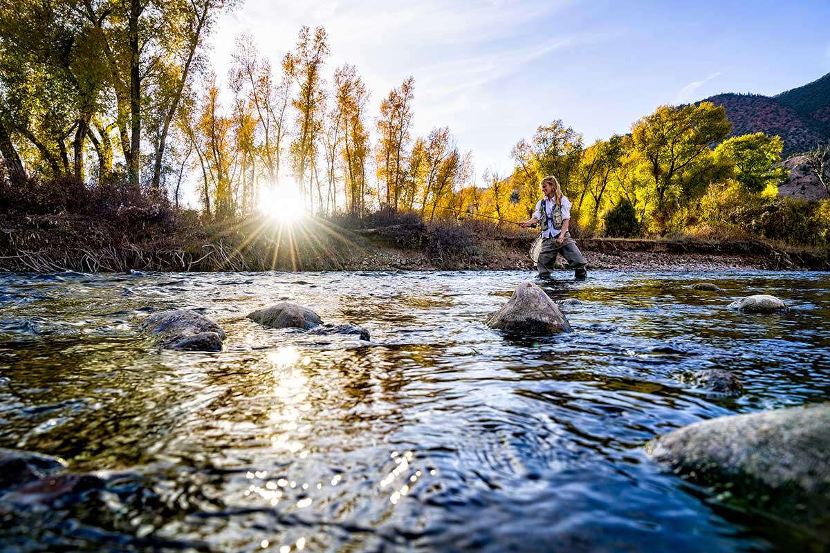 A female fly angler stands in a river and casts a line