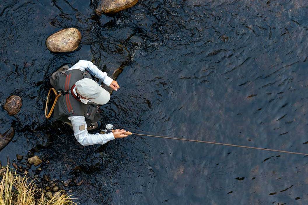 A fly fisherman viewed from overhead cast in a river