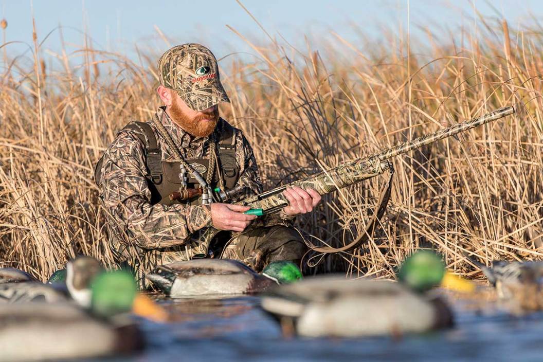Duck hunter stands in a marsh and loads his shotgun