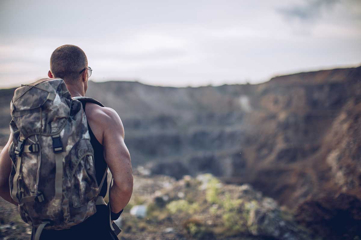 Male hiker with a camo backpack stands near a mountain