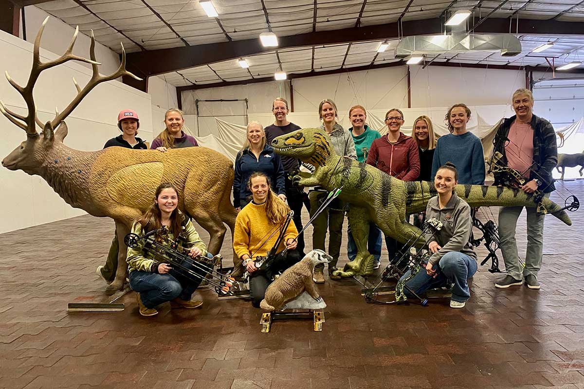 A group of women pose for a photo at an indoor archery range.