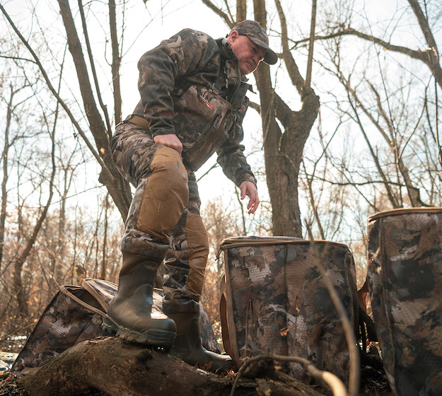 man wearing Delta Zip Waders from Sitka bends over to pick up equipment