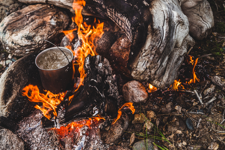 Kettle stands on fire. Cooking food at fire in wild. Beautiful big log burns in bonfire close-up. Survival in wild nature. Wonderful flame with caldron. Pot is on flames. Campfire background.