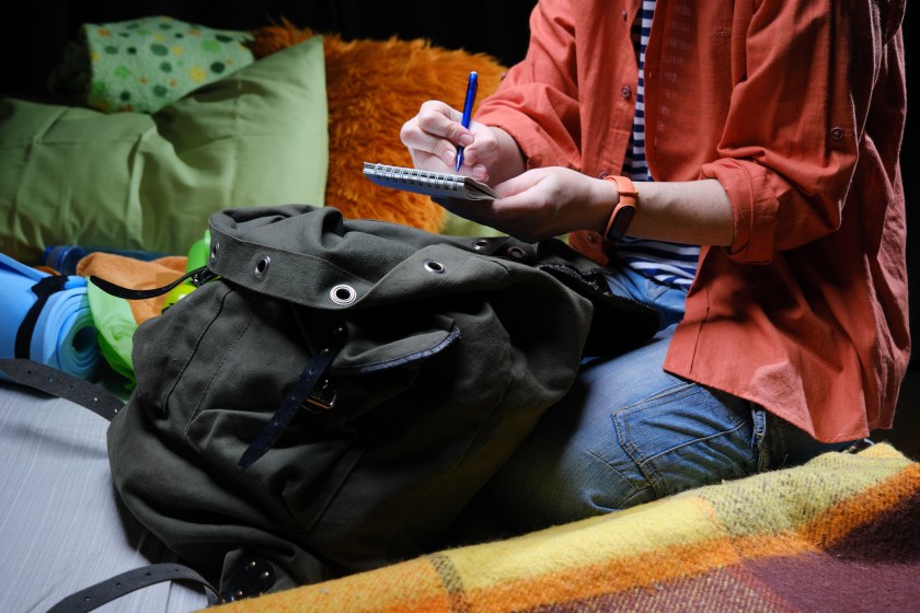 Mature person is sitting on bed and packing big rucksack for hiking