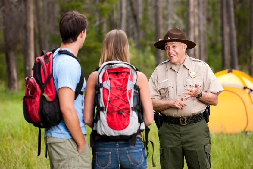 A friendly park ranger stops to talk to two backpackers near their tent in the woods