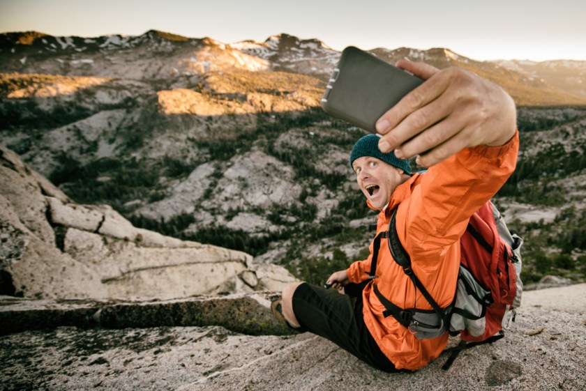 A man takes a selfie on a cliff in the backcountry