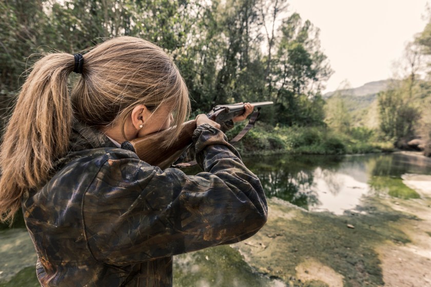 A woman hunter taking aim with her shotgun.