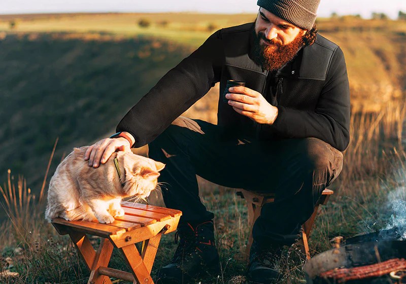 Person petting a cat on a table in a field while wearing a Tidewe jacket