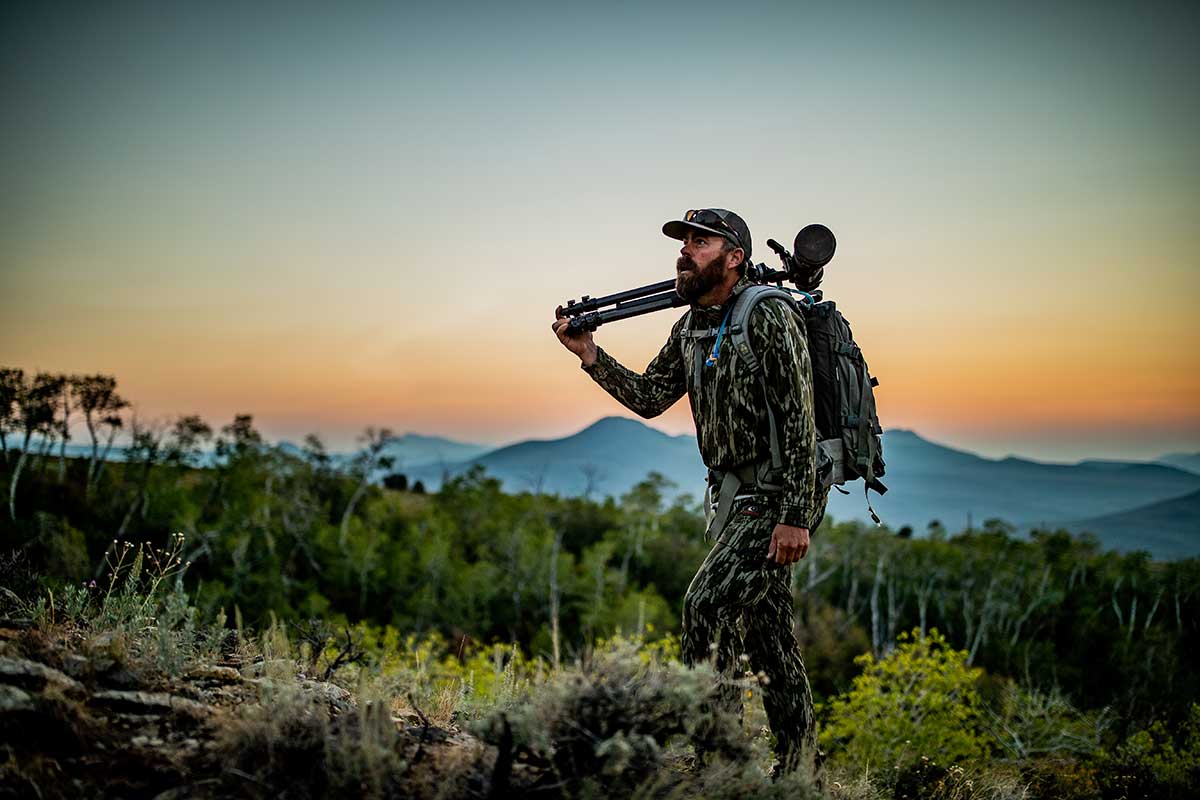 Hunter hikes up a hill while holding a spotting scope.