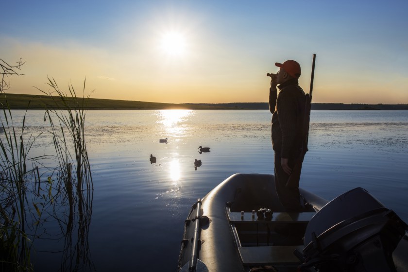 A duck hunter calling to waterfowl from a raft on a lake.