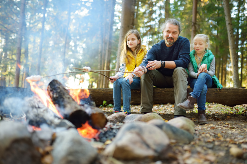 a dad and two kids sit by a fire