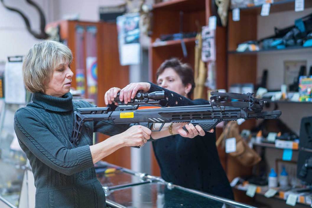 Two women inspect a crossbow inside a sporting goods store.