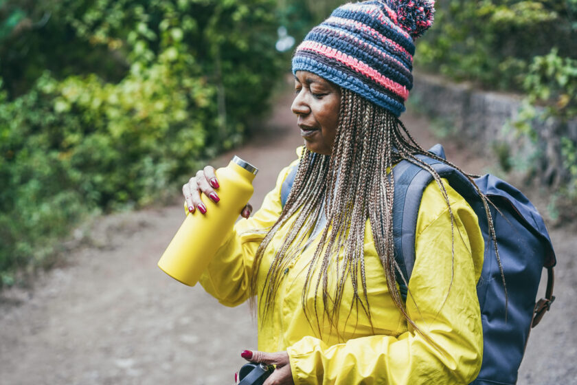 Older black woman drinking water during a hike in the woods 