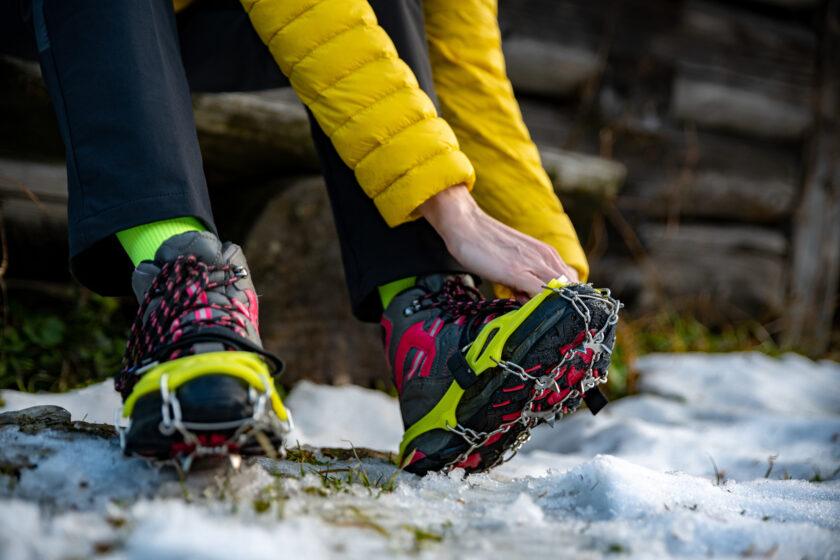 Woman hiker putting  crampons on her boots before a winter hike