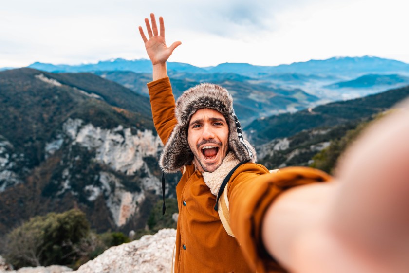 man taking selfie at the top of a mountain on a hike