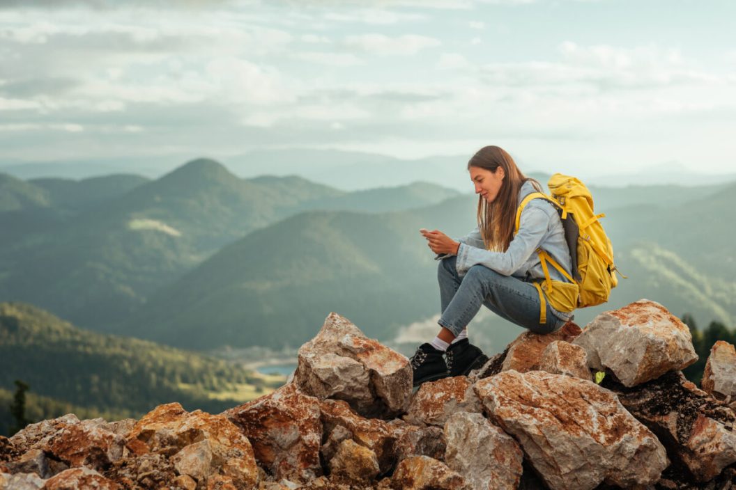Girl on her phone posting to social media on a mountain top after a hike