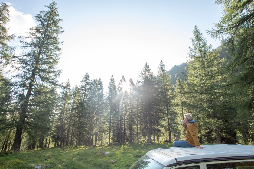 He enjoys a coffee and looks out towards lush forest surrounding