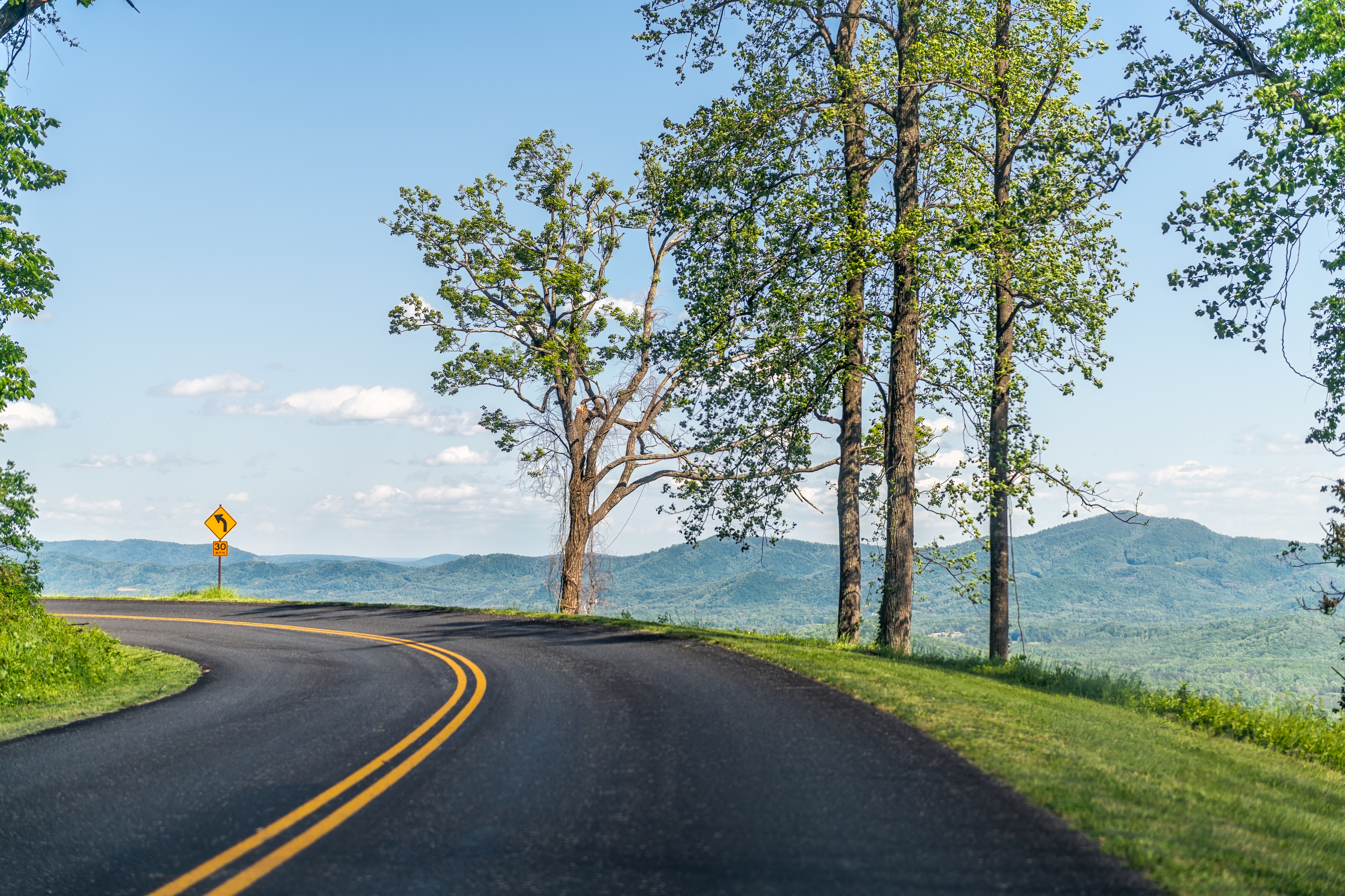 Car pov point of view driving on winding road curve road in Appalachian mountains Blue Ridge parkway in Virginia with paved asphalt road and blue sky trees