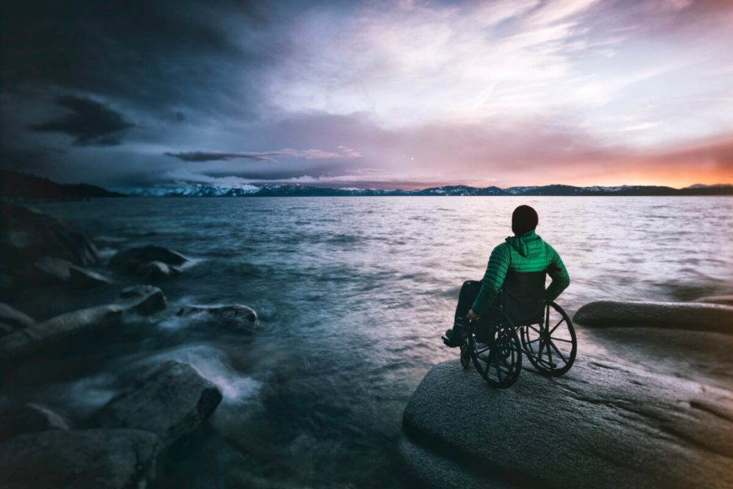 person in wheelchair out on the rocks next to the ocean, gazing at a beautiful sunset