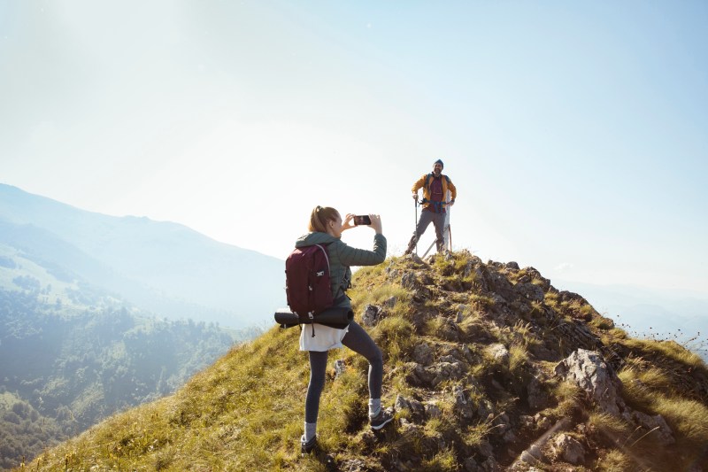 Young couple taking photos on their phone at the top of a mountain for social media