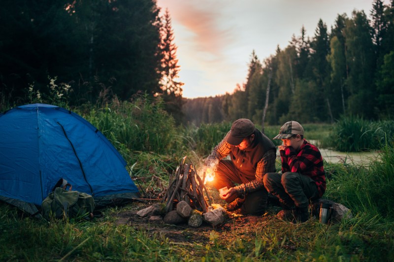Father and son camping in the backcountry by a river with a tent and a campfire, practicing leave no trace principles