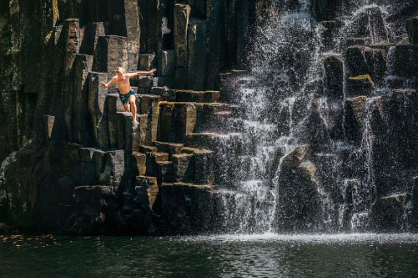 Teenage boy jumping in waterfall lake
