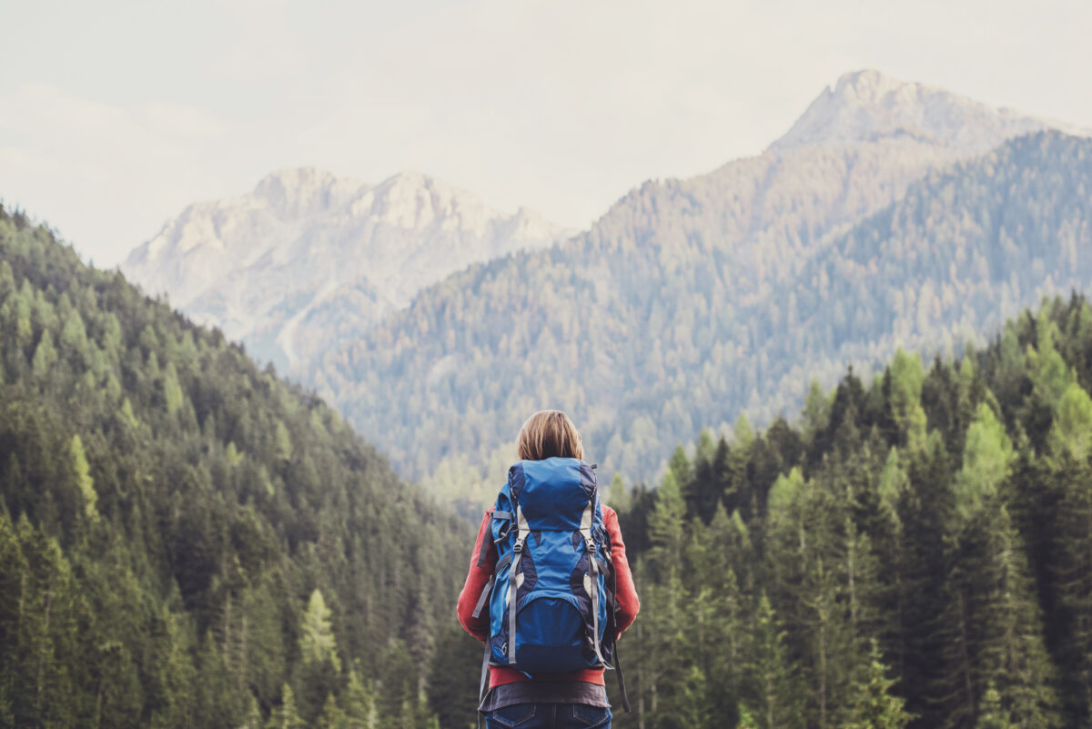 Woman hiking with background of mountains and trees, with a backpack on